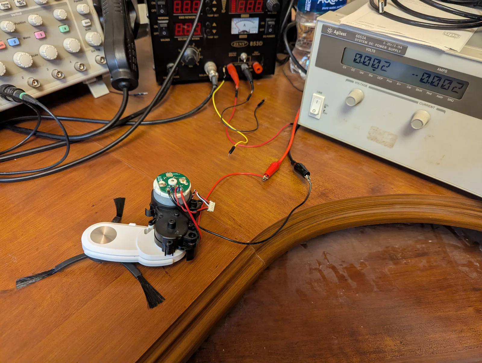 Dreame extendable side brush assembly on the bench wired to a DC power supply, showing its gearbox and sensor PCB